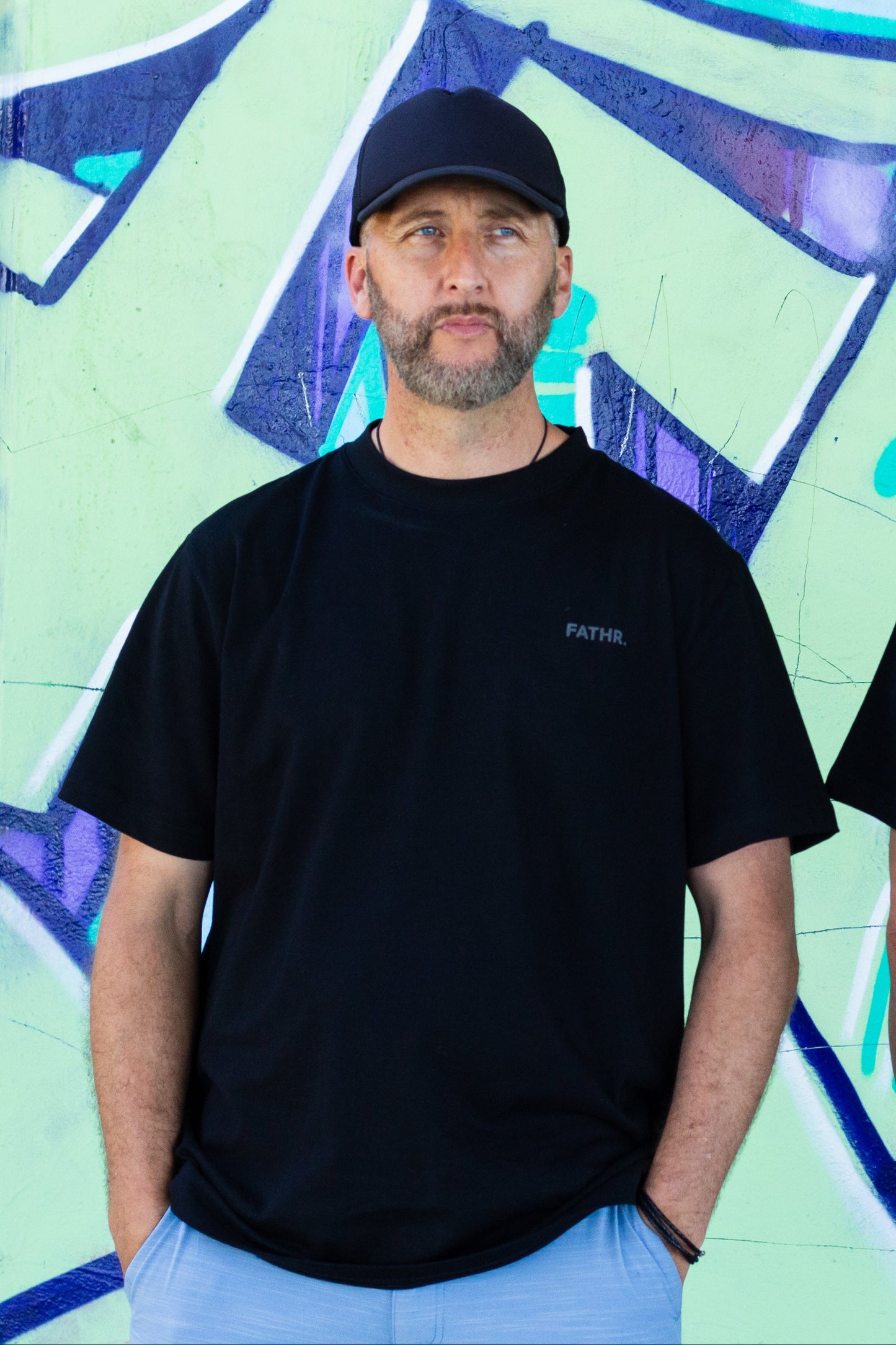 Father wearing black FATHR  t-shirt in front of a colorful graffiti wall.